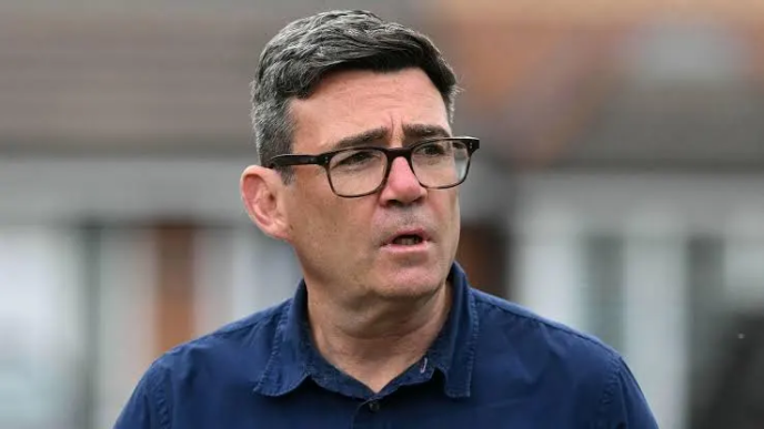 Retrato del primer ministro británico Andy Burnham con gafas y camisa azul.