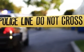 Cinta amarilla de precaución policial en la escena de un crimen con una patrulla al fondo
