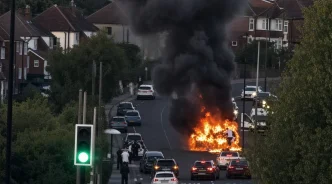 Coche envuelto en llamas y denso humo negro en medio de una carretera residencial.