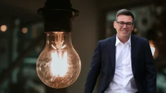 Composición con la imagen de Andy Burnham a la derecha y una bombilla encendida en primer plano a la izquierda.