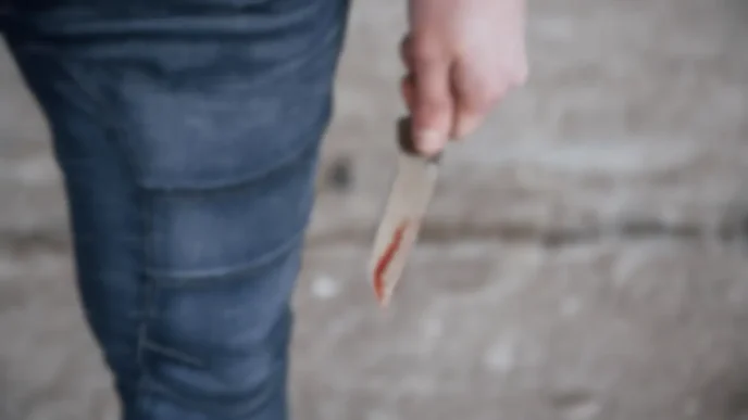 Mano sosteniendo un cuchillo ensangrentado sobre un fondo desenfocado.