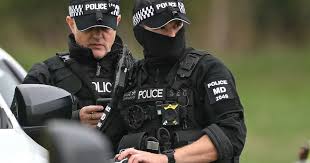 Dos agentes de la Policía Metropolitana de Londres esposando a un detenido encapuchado durante una redada policial.