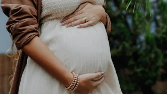 Primer plano de las manos de una mujer embarazada sosteniendo su vientre sobre un vestido blanco.