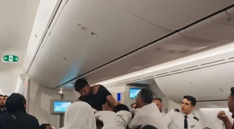 Un hombre con la camiseta rota forcejea con otros pasajeros y la tripulación dentro de la cabina de un avión.