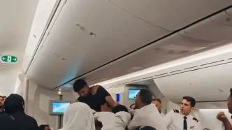 Un hombre con la camiseta rota forcejea con otros pasajeros y la tripulación dentro de la cabina de un avión.