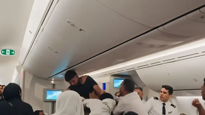 Un hombre con la camiseta rota forcejea con otros pasajeros y la tripulación dentro de la cabina de un avión.