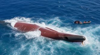 Casco de un barco semihundido en mar abierto rodeado de fuerte oleaje durante las labores de rescate.