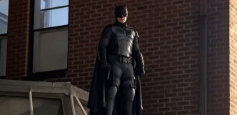 Hombre disfrazado con el traje táctico de Batman de pie sobre una estructura junto a una pared de ladrillos.Hombre disfrazado con el traje táctico de Batman de pie sobre una estructura junto a una pared de ladrillos.