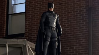 Hombre disfrazado con el traje táctico de Batman de pie sobre una estructura junto a una pared de ladrillos.Hombre disfrazado con el traje táctico de Batman de pie sobre una estructura junto a una pared de ladrillos.