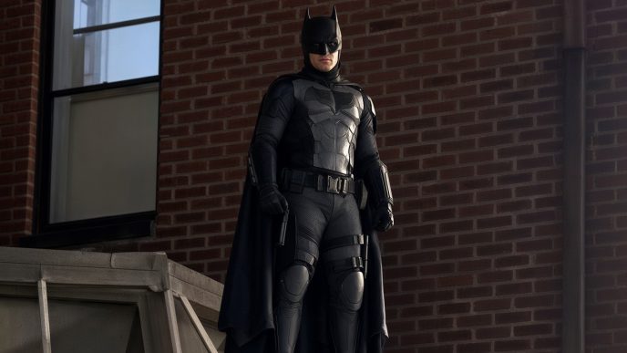 Hombre disfrazado con el traje táctico de Batman de pie sobre una estructura junto a una pared de ladrillos.Hombre disfrazado con el traje táctico de Batman de pie sobre una estructura junto a una pared de ladrillos.