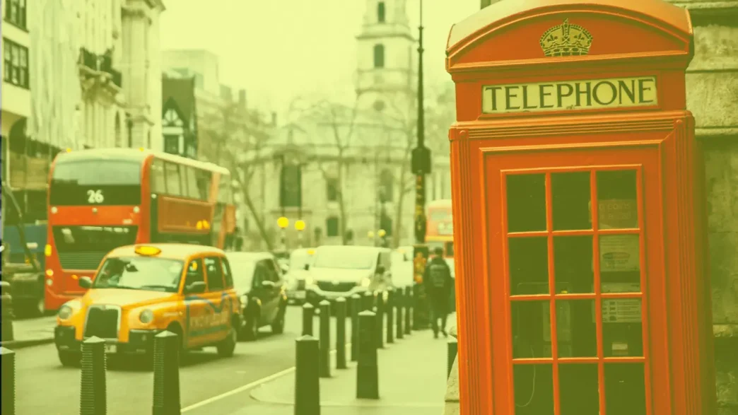 Icónica cabina telefónica roja británica y un taxi amarillo en una calle de Londres bajo un tono cálido y soleado.