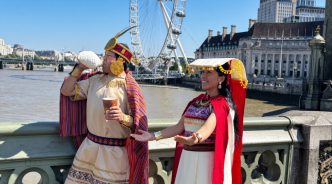 Dos personas vestidas con trajes tradicionales andinos en un puente de Londres frente a la rueda del London Eye.