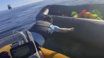 Hombre inclinado desde una pequeña embarcación rajando el lateral de una lancha neumática de rescate en el mar.