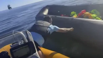Hombre inclinado desde una pequeña embarcación rajando el lateral de una lancha neumática de rescate en el mar.