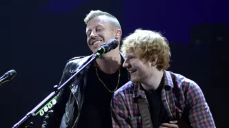 Ed Sheeran tocando la guitarra junto al rapero Macklemore sonriendo en un escenario.