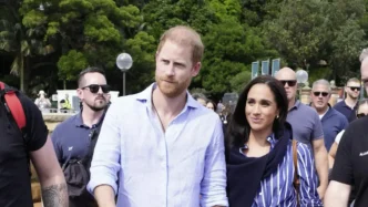 El príncipe Harry y Meghan Markle caminando juntos al aire libre rodeados de público y personal de seguridad.