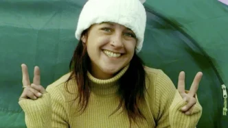 Joanne Sheen sonriendo con un gorro lana blanco y haciendo la señal de la victoria con ambas manos.