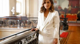 Laura Sarabia vestida con un traje blanco posando junto a una barandilla en un edificio institucional.