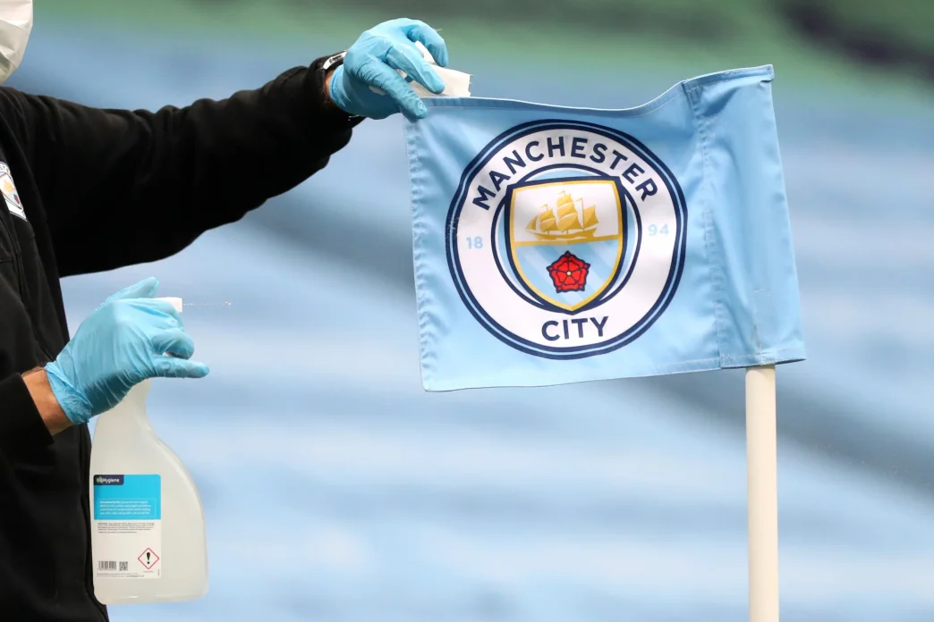 Banderín de córner con el escudo del Manchester City siendo desinfectado por un operario con guantes.