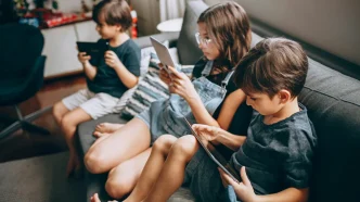 Niños y adolescentes sentados en un sofá utilizando tabletas y teléfonos móviles.