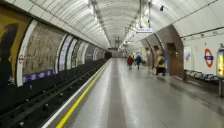 Anden subterraneo iluminado de una estacion del metro de Londres con vias a la izquierda y senalizacion icnica.