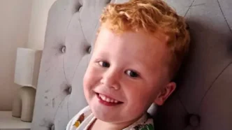 Retrato del niño Noah Woods sonriendo a la cámara apoyado en un respaldo gris.