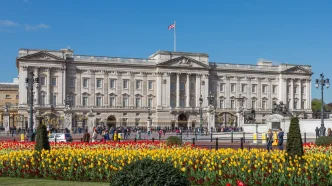 Fachada principal del Palacio de Buckingham con flores en los jardines y la bandera británica ondeando en el tejado