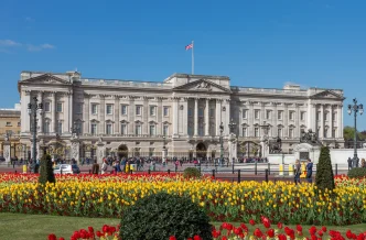 Fachada principal del Palacio de Buckingham con flores en los jardines y la bandera británica ondeando en el tejado