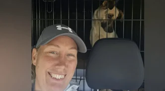 Selfie de Rachael Harvey-Purkiss sonriendo dentro de un vehículo con un perro rescatado en un transportín detrás.