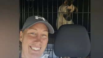 Selfie de Rachael Harvey-Purkiss sonriendo dentro de un vehículo con un perro rescatado en un transportín detrás.