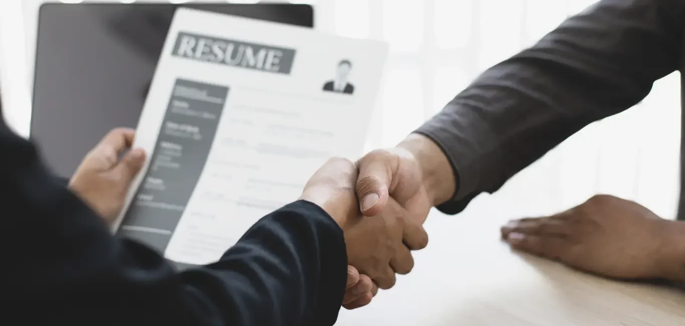 Dos profesionales estrechándose la mano durante una entrevista de trabajo con un currículum en primer plano