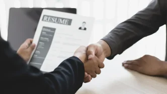 Dos profesionales estrechándose la mano durante una entrevista de trabajo con un currículum en primer plano