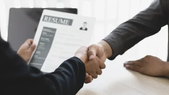 Dos profesionales estrechándose la mano durante una entrevista de trabajo con un currículum en primer plano