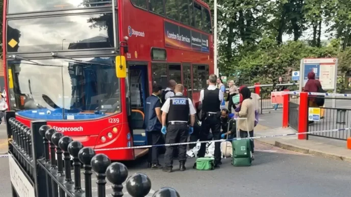 Agentes de policía y servicios de emergencia atendiendo a un peatón en el suelo junto a un autobús rojo de dos pisos acordonado en Walthamstow.