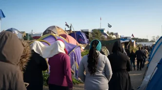 Grupo de migrantes caminando de espaldas por un campamento informal de tiendas de campaña en el norte de Francia.