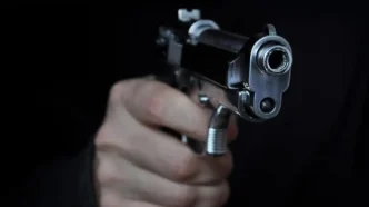 Mano empuñando una pistola plateada apuntando de frente hacia la cámara sobre fondo negro.