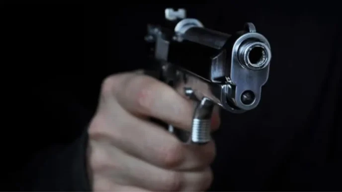 Mano empuñando una pistola plateada apuntando de frente hacia la cámara sobre fondo negro.