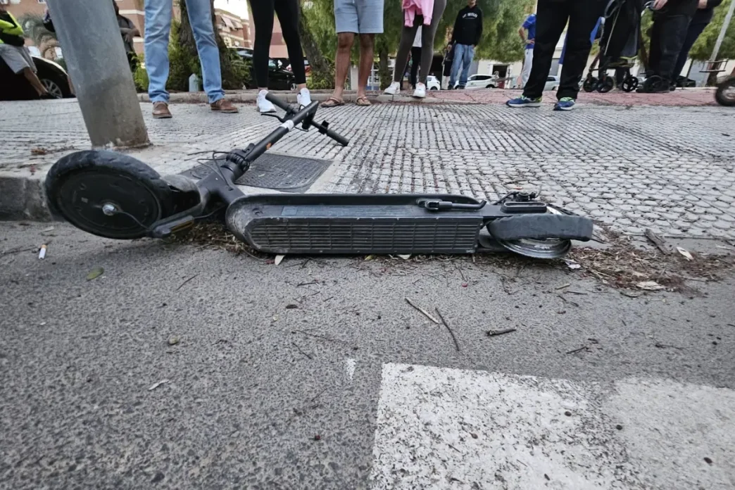 Patinete o vehículo ligero tumbado en la acera tras un accidente de tráfico con testigos alrededor.