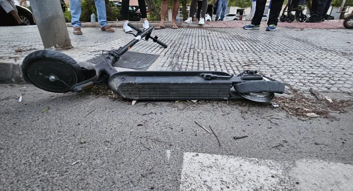 Patinete o vehículo ligero tumbado en la acera tras un accidente de tráfico con testigos alrededor.