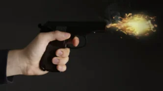 Mano sosteniendo una pistola en el momento exacto en que se produce un disparo con llamarada en la boca del cañón.