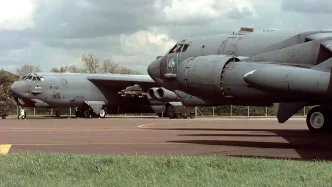 Dos bombarderos militares pesados estacionados en la plataforma de asfalto de una base aérea bajo un cielo nublado.