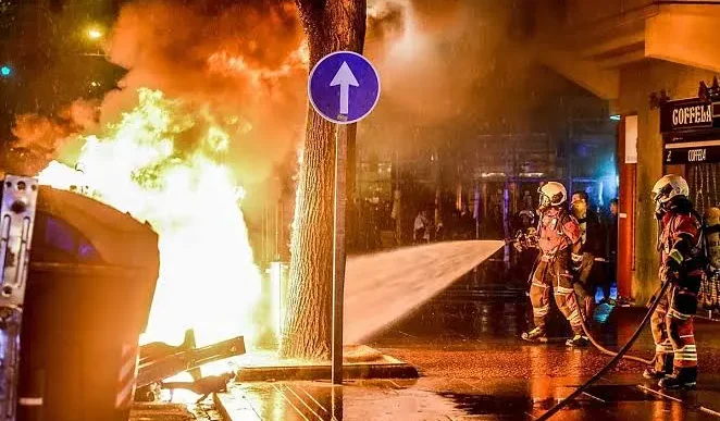 Contenedores incendiados y vehículos calcinados durante los disturbios nocturnos en el centro urbano.