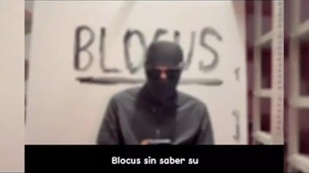 Captura de vídeo de un individuo con la cara tapada frente a una pintada con la palabra Blocus.