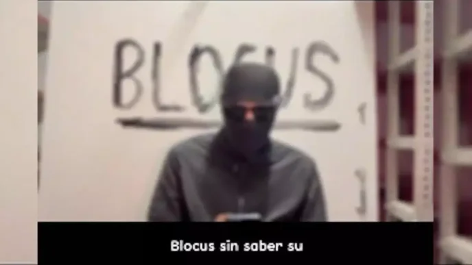 Captura de vídeo de un individuo con la cara tapada frente a una pintada con la palabra Blocus.