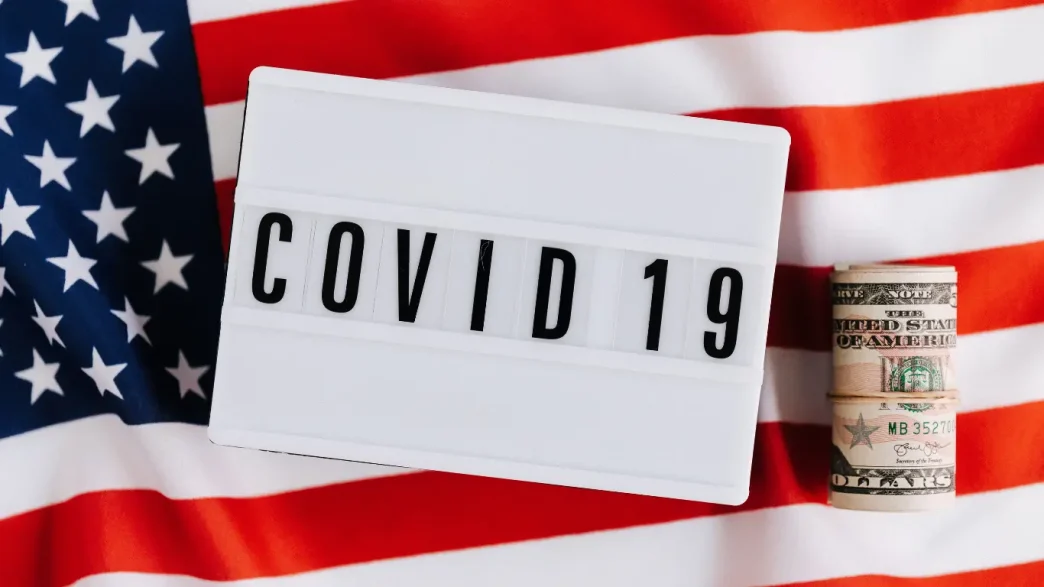 Letrero con el texto COVID 19 sobre la bandera de Estados Unidos y fajos de dólares.