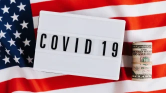 Letrero con el texto COVID 19 sobre la bandera de Estados Unidos y fajos de dólares.