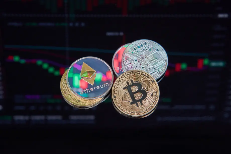 Monedas físicas de criptomonedas como Bitcoin y Ethereum sobre un fondo de gráficos bursátiles digitales.
