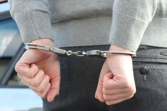 Persona con jersey gris y pantalones oscuros inmovilizada mediante grilletes metálicos en las muñecas a la espalda.