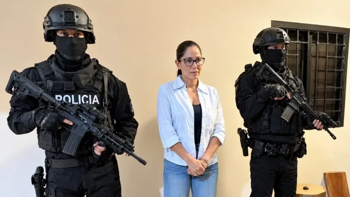 Dos agentes de la policía táctica con pasamontañas negros y fusiles de asalto flanquean a una mujer con gafas en el interior de una sala.