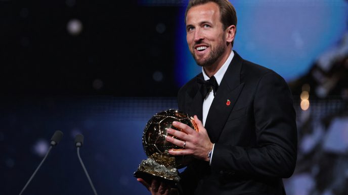 Harry Kane sonriendo en el escenario mientras sostiene el trofeo del Balón de Oro 2026 vistiendo un esmoquin negro.